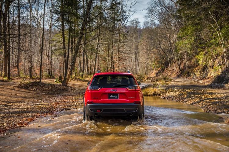 jeep cherokee trailhawk fording a stream in the forest