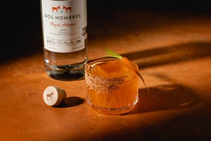 Dos Hombres Mezcal bottle with Sweet Lips cocktail featuring chili salt rim and carrot garnish